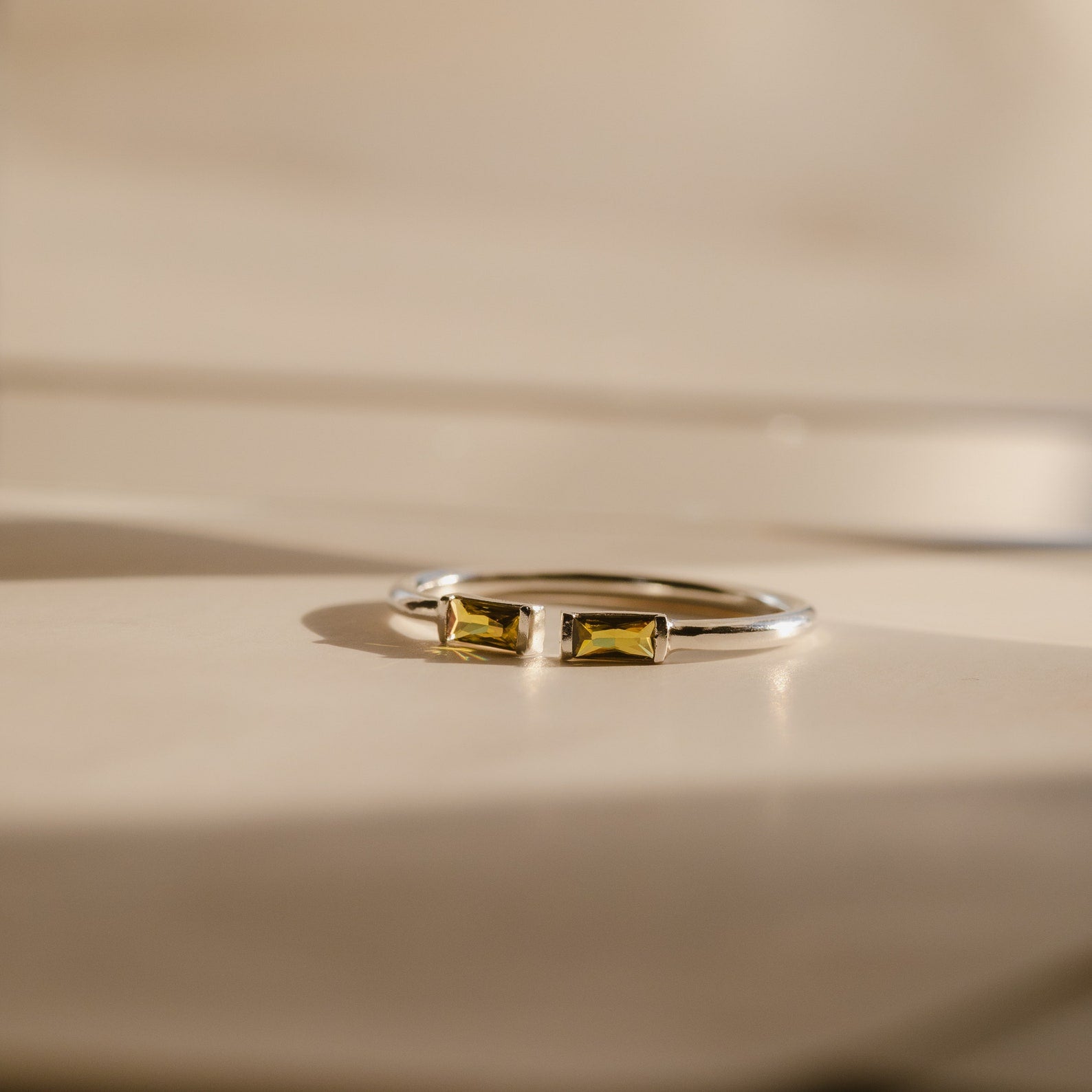 A Duo Baguette Birthstone Ring with two rectangular yellow stones sits on a beige surface, ideal for a personalized gift or displaying your chosen birthstones.