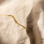 The Morse Code Necklace features delicate gold beads and bars, displayed on a textured light fabric. This elegant, customizable necklace makes a perfect personalized gift.