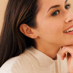 Woman with long brown hair wearing a beige turtleneck and Trio Beaded Bar Studs, smiling gently—perfect minimalist earrings for everyday wear.