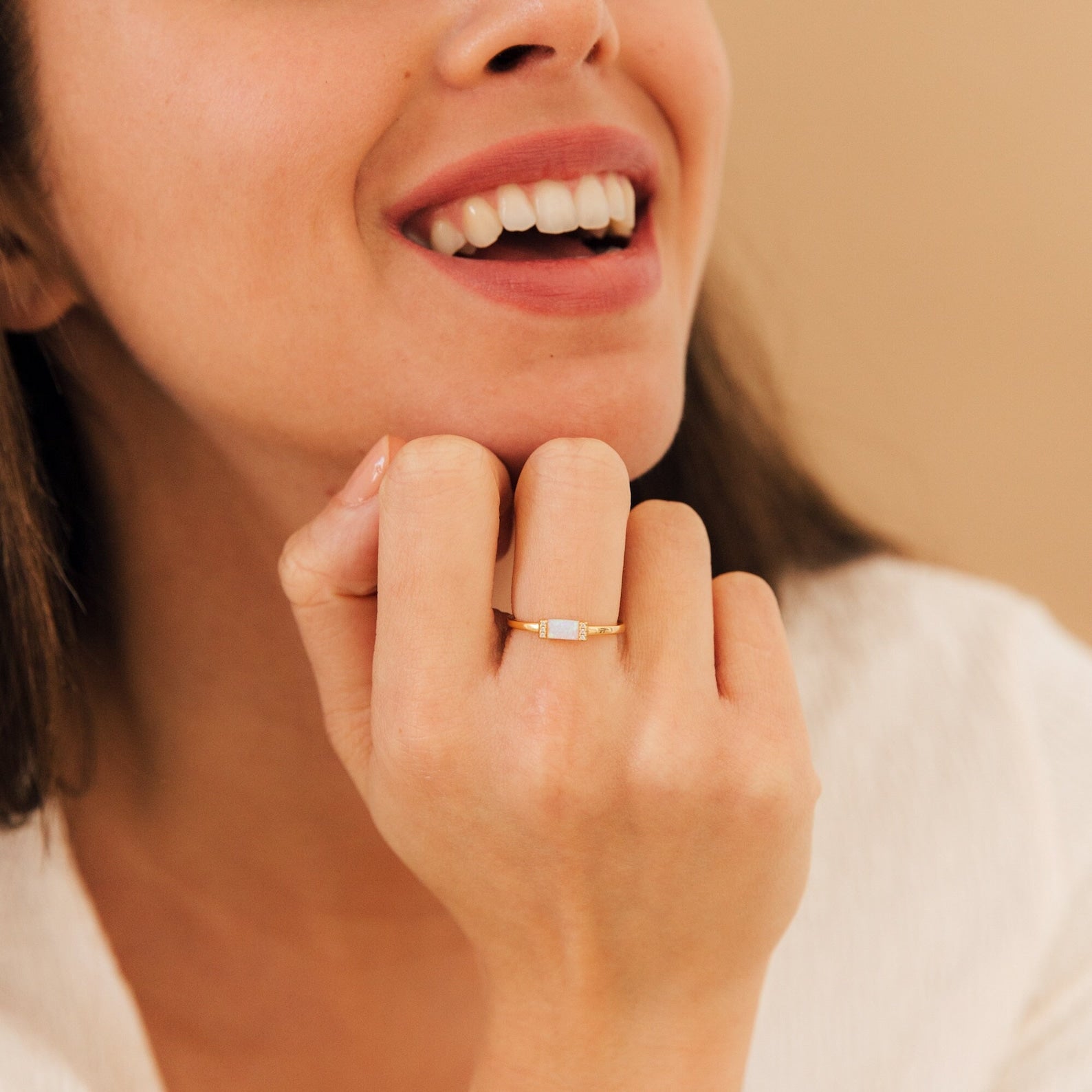 A woman smiles in a close-up, wearing the Kiera Opal Baguette Ring—a dainty ring with a rectangular white opal stone on her finger.