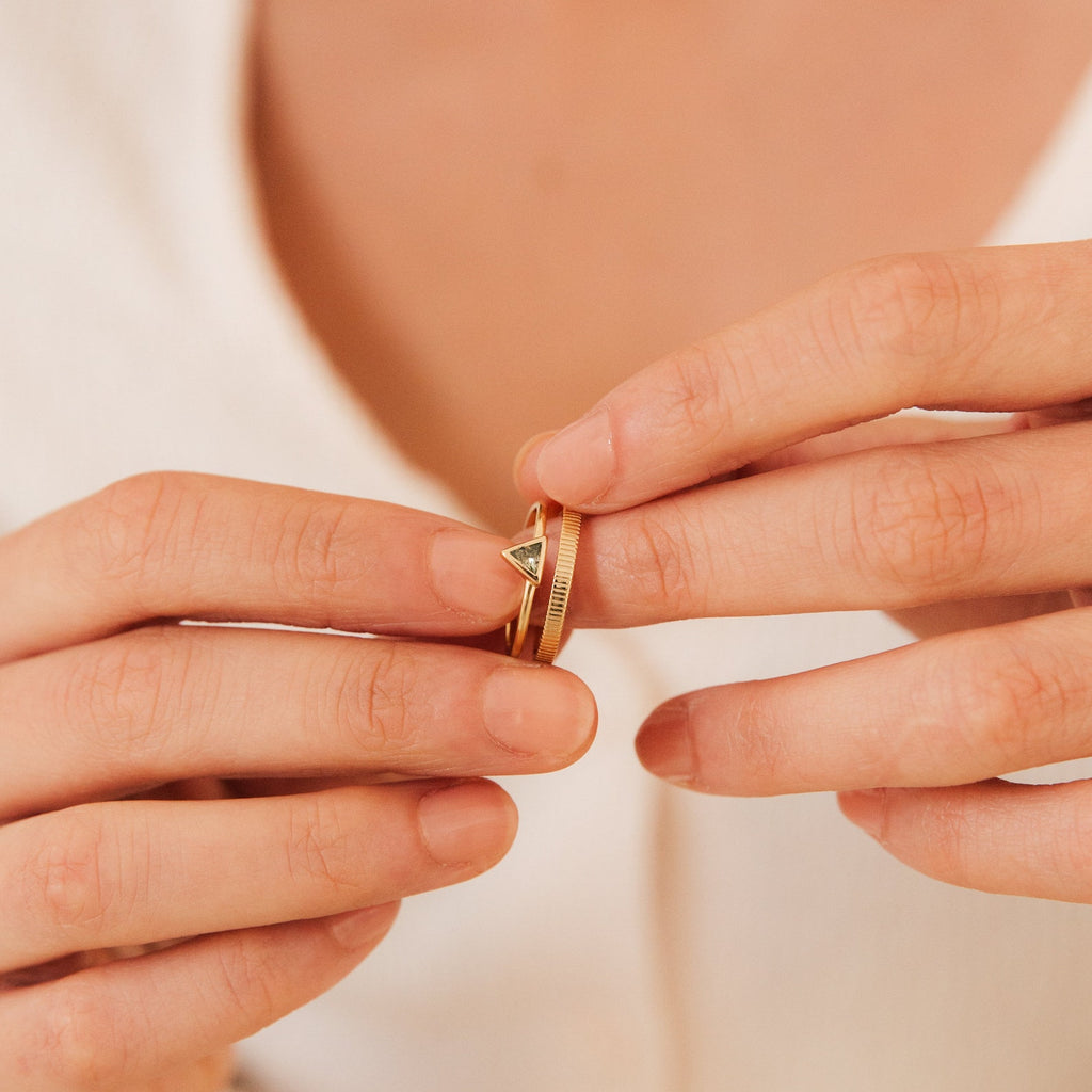Close-up of hands sliding the Jaida Peridot Duo Ring, a gold Art Deco style piece with two small triangle-shaped stones, onto a finger.