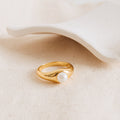 The Penelope Pearl Signet Ring, showcasing a single freshwater pearl, is displayed on textured beige fabric next to a white ceramic dish.