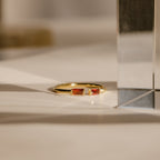 The Duo Baguette Birthstone Ring, featuring two rectangular red stones, rests on a white surface in gentle sunlight—a beautiful choice for a personalized gift.