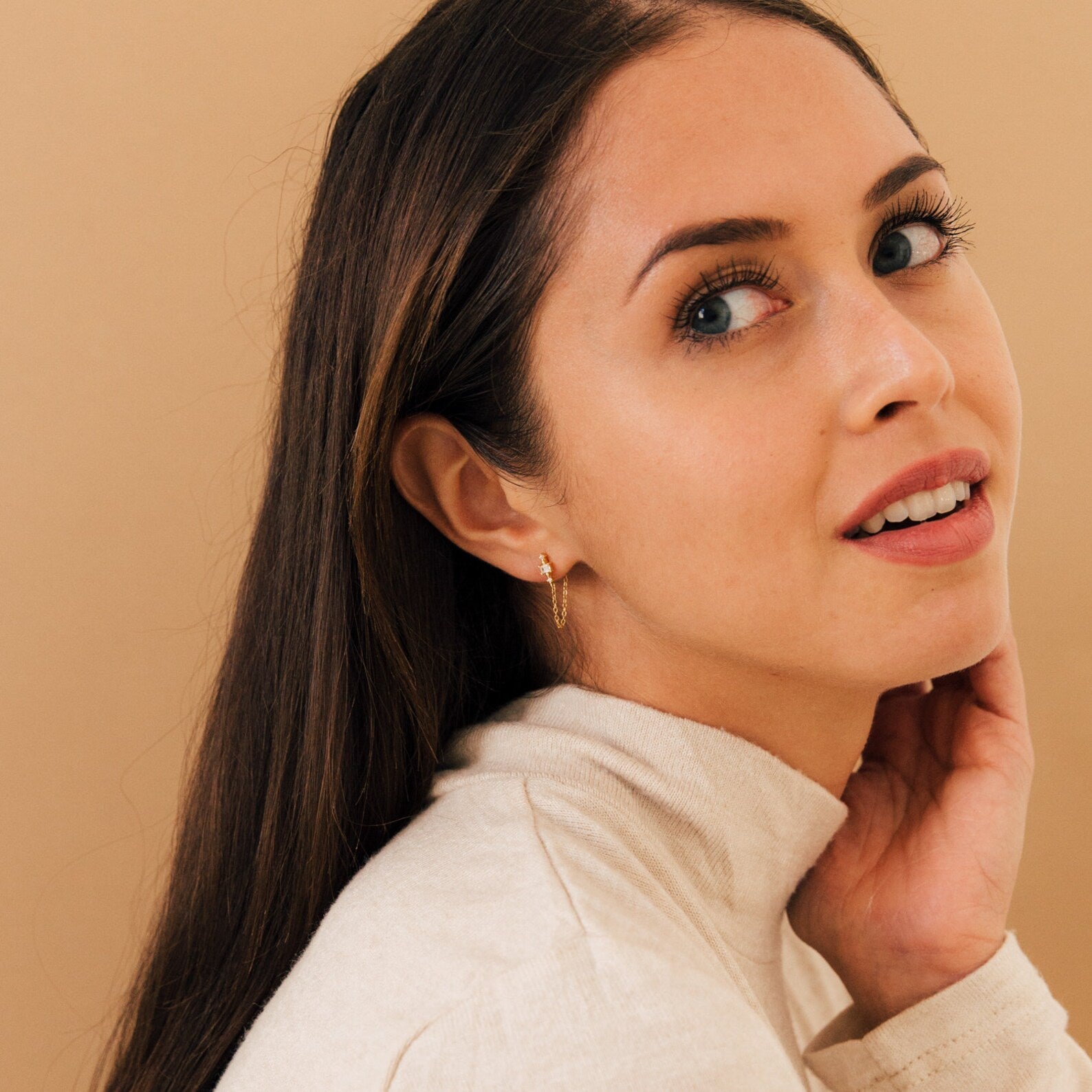 A woman with long hair and a white turtleneck models the Florence Diamond Chain Earrings, adding a touch of modern elegance to her look.