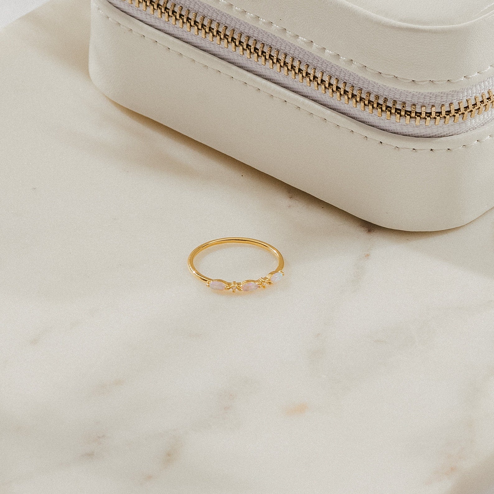 Alessia Trio Opal Ring in gold displayed on a marble surface beside a cream jewelry case, showcasing its opals and diamond accents.