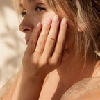 A blonde woman gently touches her face, showcasing the Skinny Stacking Rings Set on her fingers in soft sunlight.