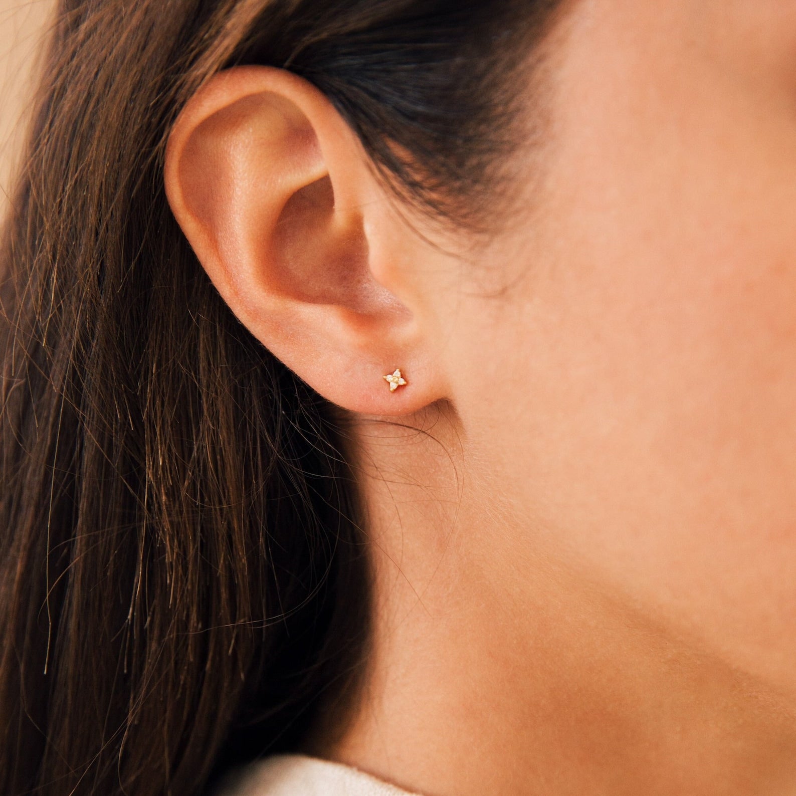 Close-up of a woman wearing a Hera Flower Stud Earrings in gold on her earlobe, with straight brown hair tucked behind her ear.