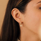 Close-up of a woman's ear wearing Aleah Opal Evil Eye Huggies, featuring a diamond-shaped pendant that blends classic style with modern elegance.