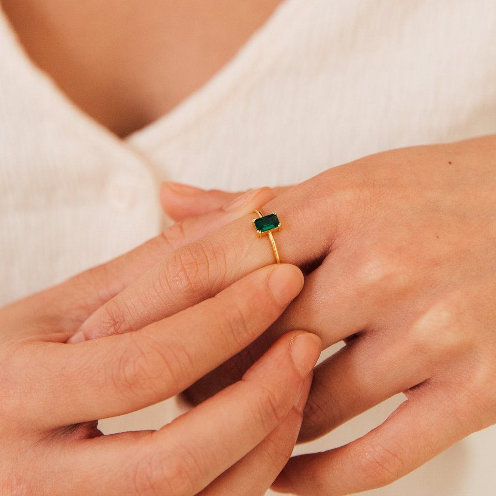 A person wears the Harley Emerald Ring, featuring a rectangular green stone, and adjusts it on their finger.