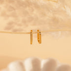 Large Ribbed Link Hoops hang from a thin branch against a soft beige background with blurred décor, ideal for lovers of minimalist jewelry.
