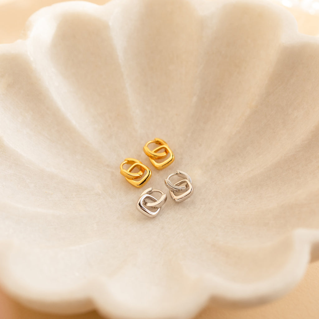 Two pairs of chic geometric gold and silver Reagan Duo Huggies, including minimalist hoops, displayed on a scalloped cream-colored dish.