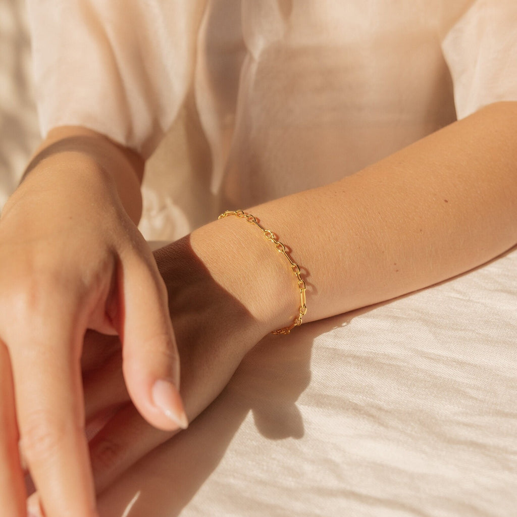 The Roxy Paperclip Chain Bracelet is shown on a wrist, delicately shining in soft sunlight with a neutral fabric backdrop.
