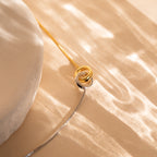 Interlocking Circles Bracelet on a beige surface with soft, wavy light reflections—a perfect anniversary gift for those who appreciate refined elegance.