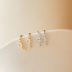 Two pairs of Amaya Marquise Threaders—one in gold, one in silver—adorned with dainty diamond clusters. These curved earrings sparkle beautifully displayed on a white surface.