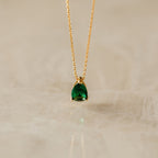 Ophelia Birthstone Necklace: a minimalist gold chain with a pear-shaped green gemstone pendant, perfect as a personalized gift or elegant birthstone necklace, displayed on a light marble surface.