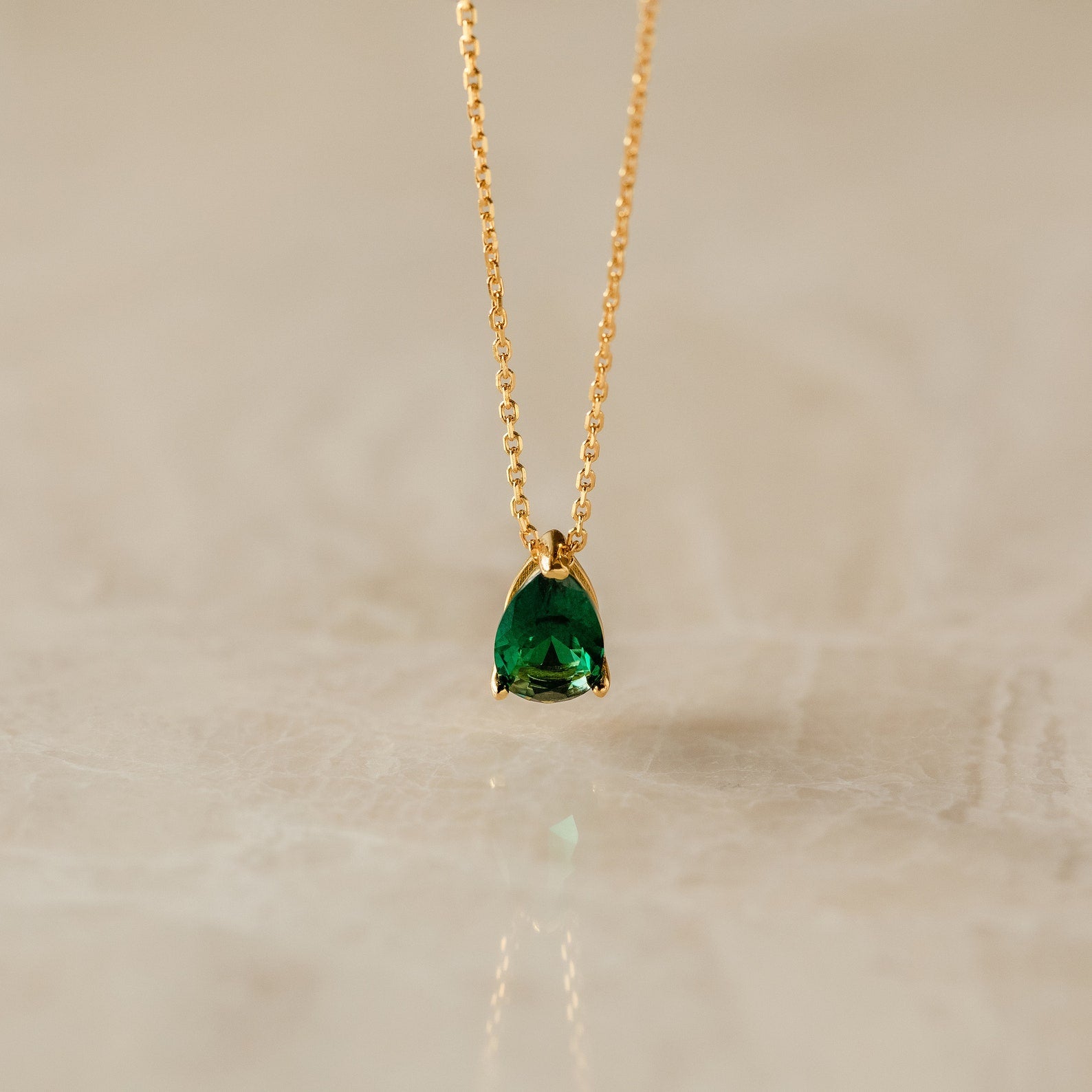 Ophelia Birthstone Necklace: a minimalist gold chain with a pear-shaped green gemstone pendant, perfect as a personalized gift or elegant birthstone necklace, displayed on a light marble surface.
