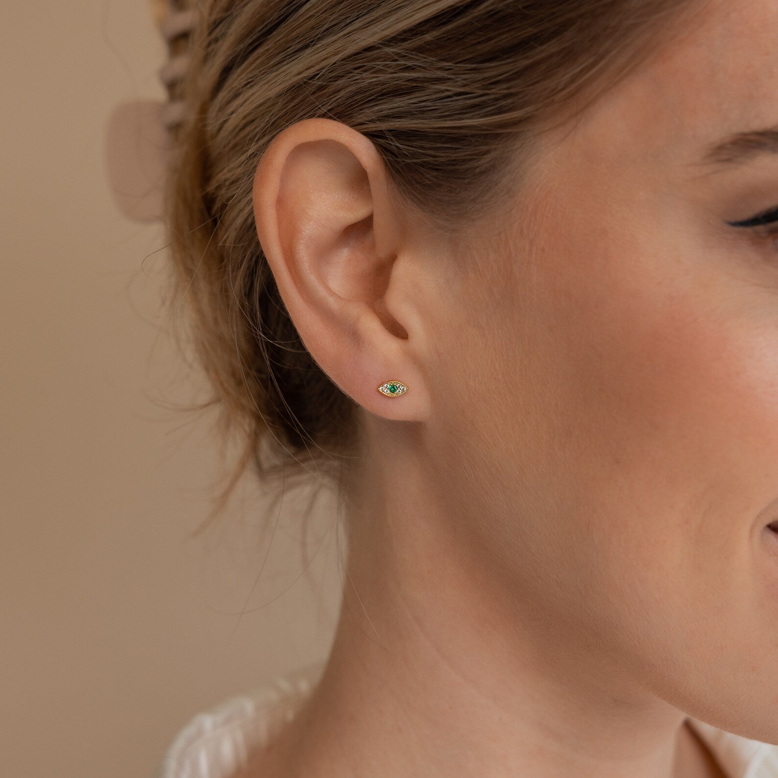 Close-up of a woman's ear adorned with Haven Emerald Eye Studs, featuring a vibrant green emerald stone at the center.
