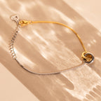 The Interlocking Circles Bracelet, featuring minimalist gold and silver rings, sits on a sunlit beige surface—an elegant anniversary gift.
