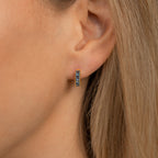 Close-up of a woman's ear wearing Genevieve Birthstone Huggies with blue gemstones—small gold earrings that make a beautiful gift for mom.