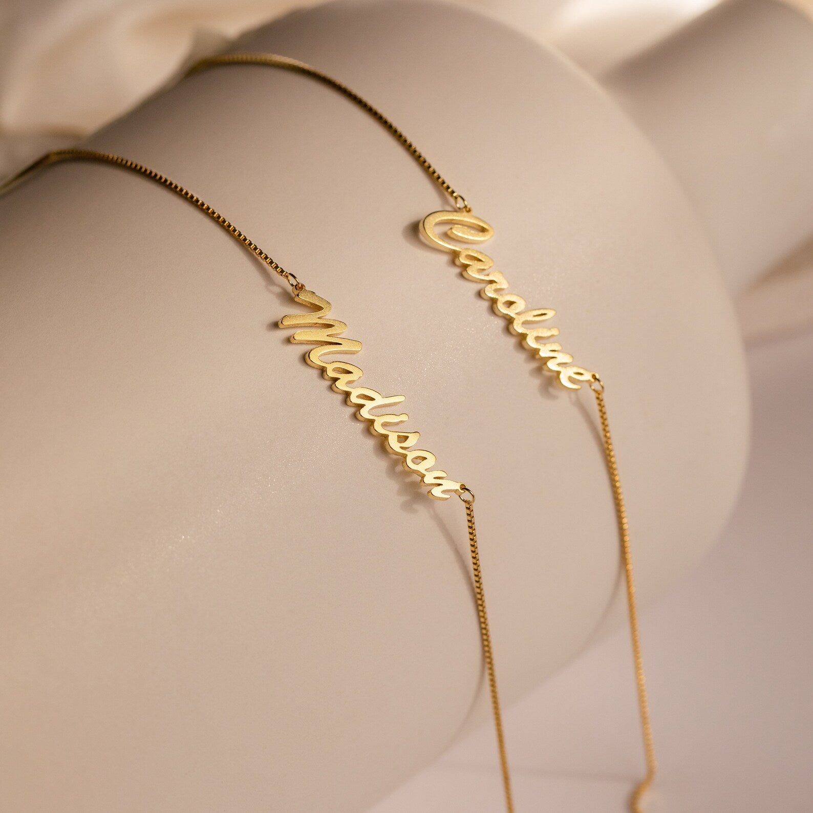 Two Casella Name Necklaces in Box Chain, customized with "Madison" and "Caroline" in delicate script font, create an elegant personalized gift shown on a white surface.