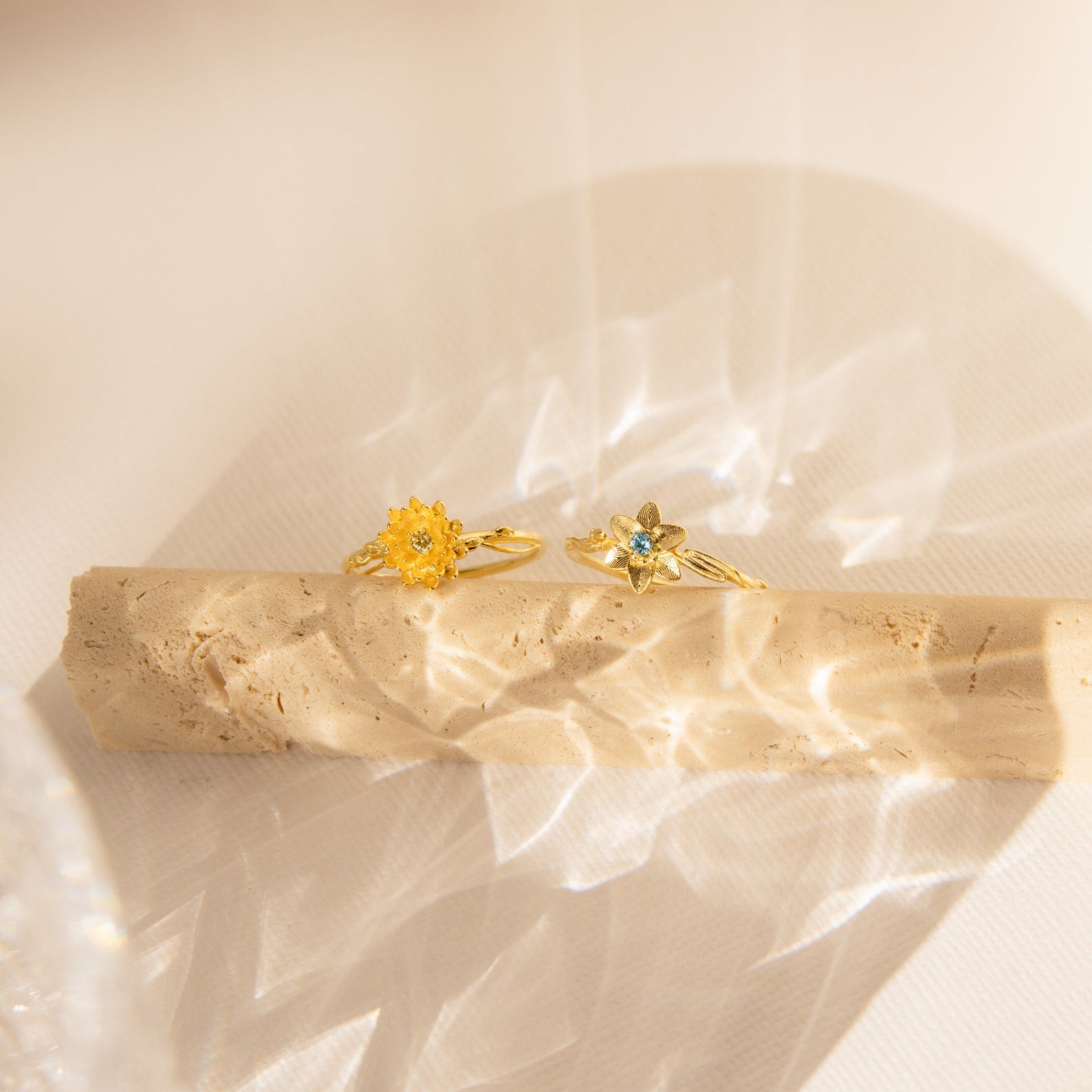 A Flower Birthstone Ring with a vintage-inspired flower design rests on a textured beige surface in soft sunlight.