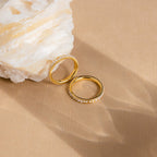 The Alicia Pearl Inlay Band, a gold stackable ring with delicate pearls, rests on a beige surface beside a large white crystal rock.