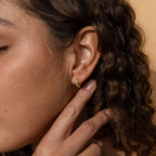 A close-up of a woman's ear wearing the Opal Inlay Huggies Set, showcasing the hoops' vibrant opal colors.