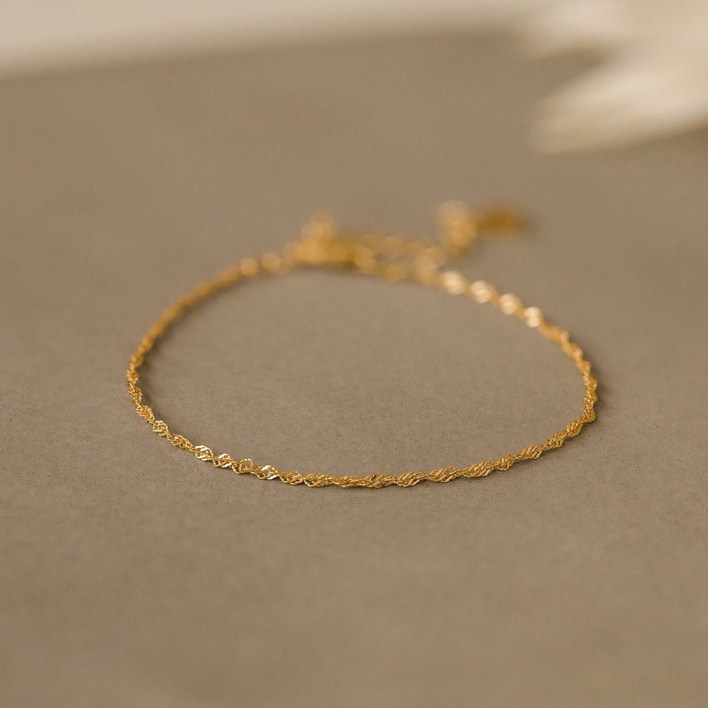 The Singapore Twist Bracelet shines on a neutral beige surface, ideal for those who appreciate dainty bracelets and minimalist elegance.