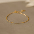 The Singapore Twist Bracelet shines on a neutral beige surface, ideal for those who appreciate dainty bracelets and minimalist elegance.