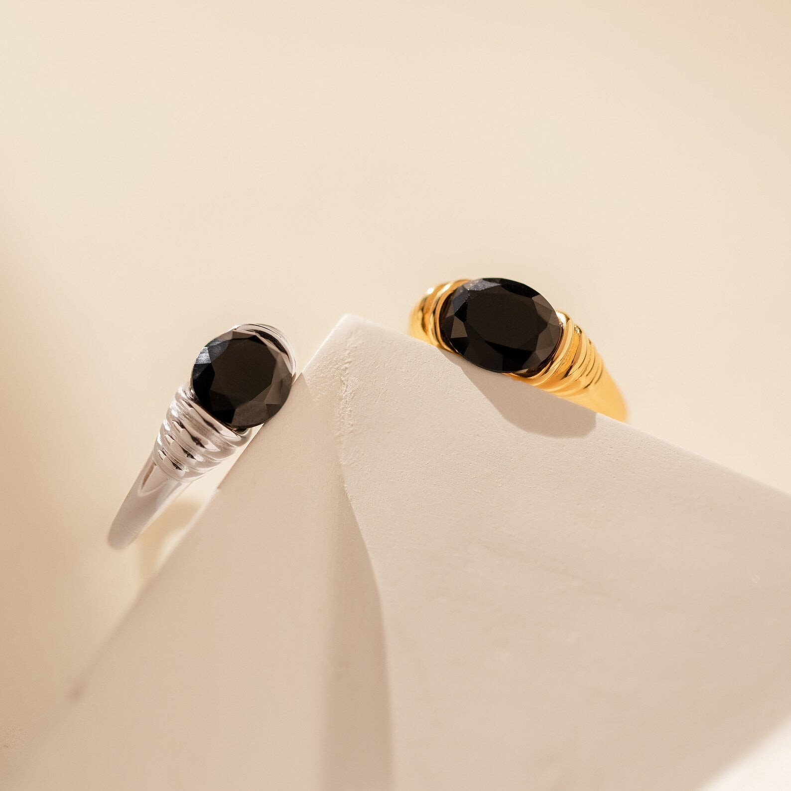 The Dusk Signet Ring, available in silver or gold with a black onyx stone, rests on a white geometric surface—ideal as statement jewelry or for adding vintage-inspired signet ring style.