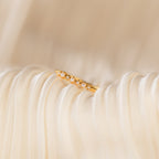 The Delicate Pearl Diamond Ring, featuring small pearls and diamonds in a gold band, rests on soft, pleated cream-colored fabric.