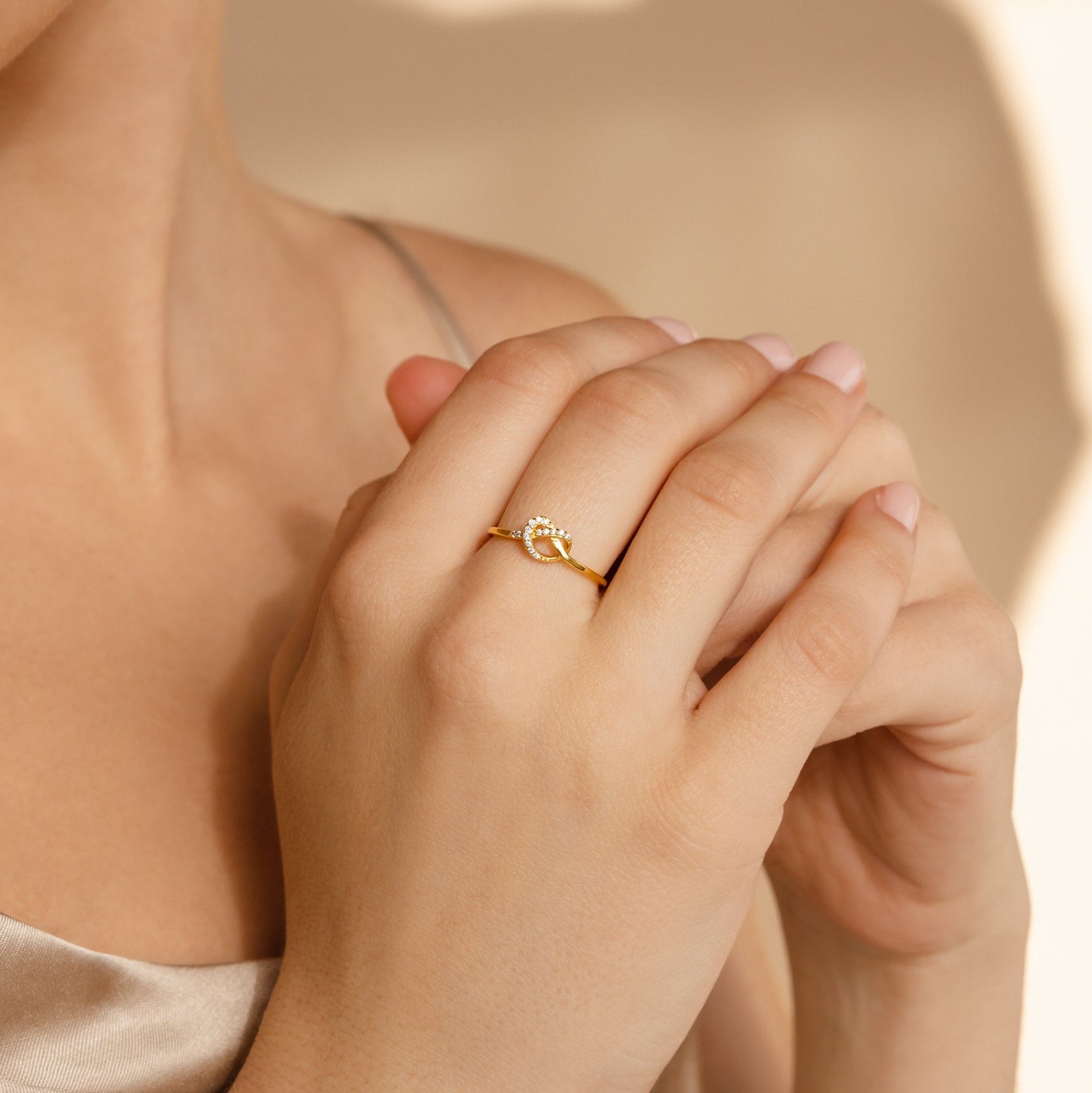 Close-up of hands with light pink nails wearing the Pave Heart Knot Ring—a sparkling, clear gemstone on the ring finger, perfect as a romantic gift or promise ring.