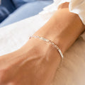 The Mini Name Bar Bracelet, featuring engraved name plates, rests on a wrist atop a white surface—an ideal personalized gift.