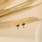 The Emily Drop Earrings in gold and black rest on dried beige palm leaves, set against a minimal, soft background—ideal statement earrings for adding a subtle hint of vintage elegance.