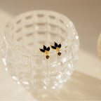 Emily Drop Earrings in gold and black are displayed on a textured clear glass container in soft light, offering a bold vintage statement to any look.