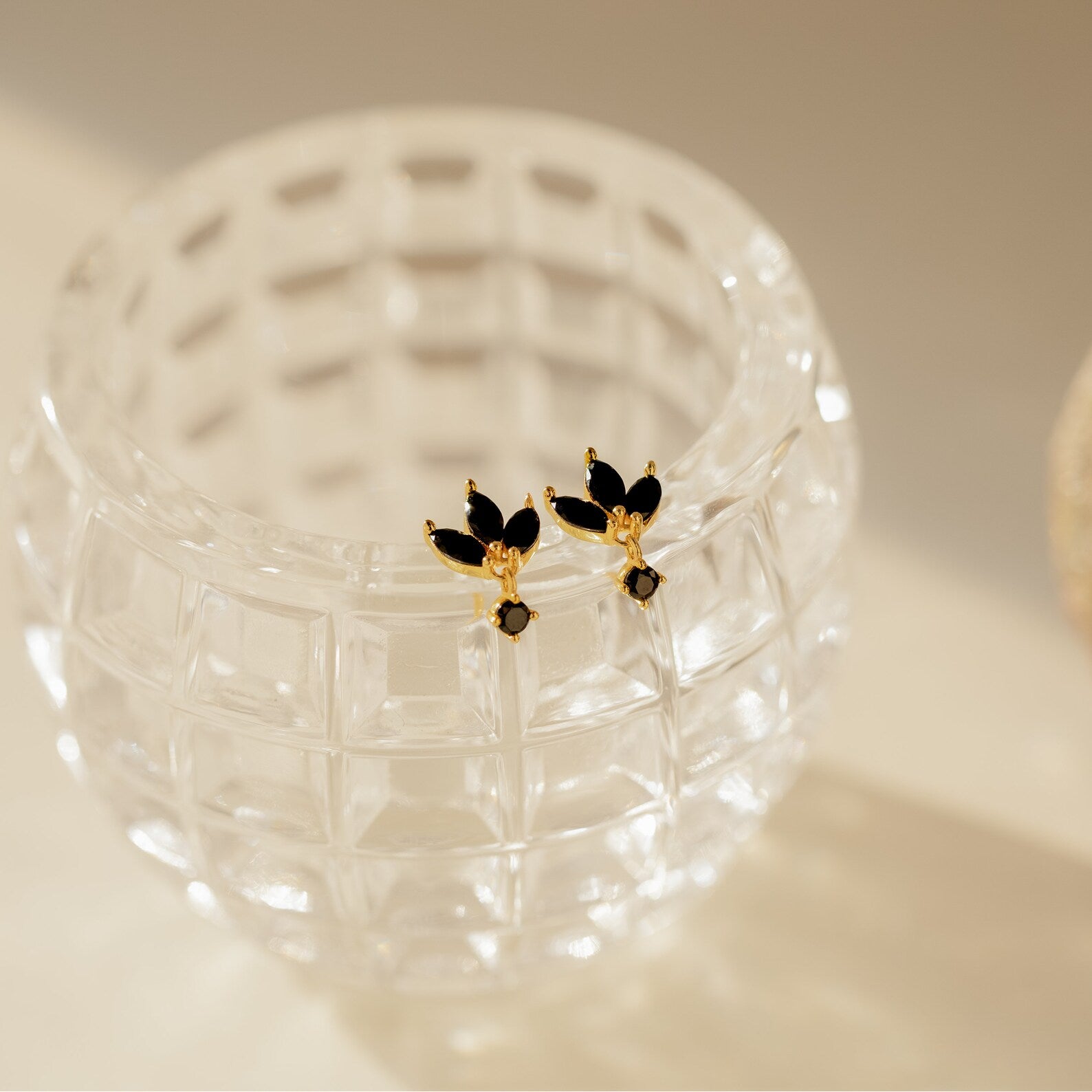 Emily Drop Earrings in gold and black are displayed on a textured clear glass container in soft light, offering a bold vintage statement to any look.
