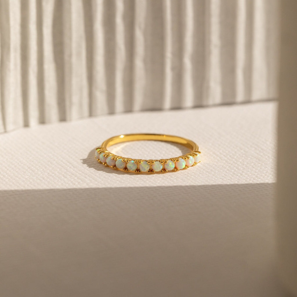 The Crescent Opal Ring features small oval opal stones set in gold, beautifully displayed on a textured white surface with soft shadows—an elegant promise ring or thoughtful anniversary gift.