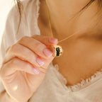 A woman wearing a cream top holds a meaningful gift—a Pearl Disc Locket Necklace featuring a gold locket with a black cat silhouette inside.