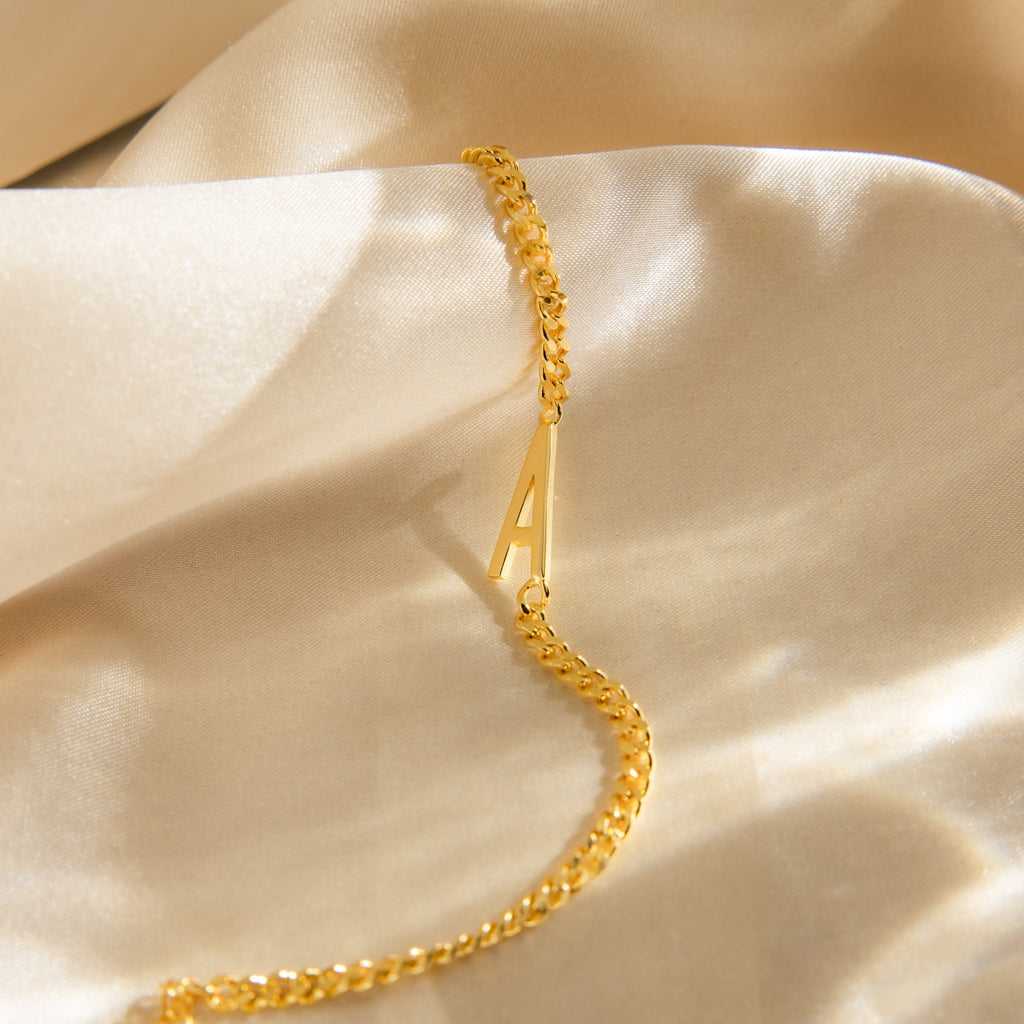 Large Letter Bracelet with a gold curb chain and A charm, displayed on soft beige satin—a stylish, personalized accessory for everyday wear.