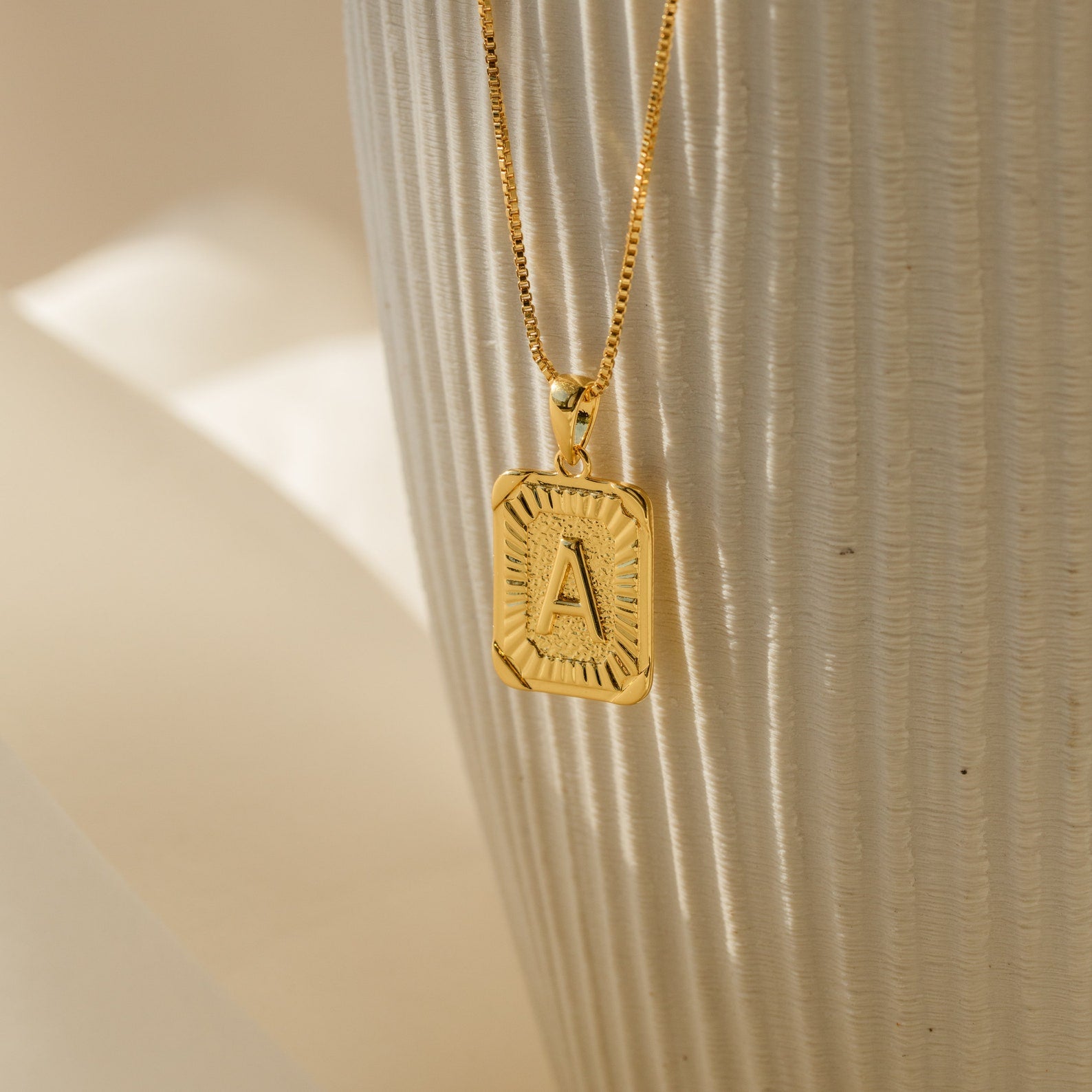 The Initial Rectangle Pendant Necklace features a gold rectangle pendant engraved with the letter A, displayed against a textured white background—an ideal personalized gift for any occasion.