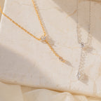 The Leena Diamond Lariat Necklace, featuring both round and marquise-shaped gemstones in a delicate lariat design, is displayed elegantly on a beige surface.