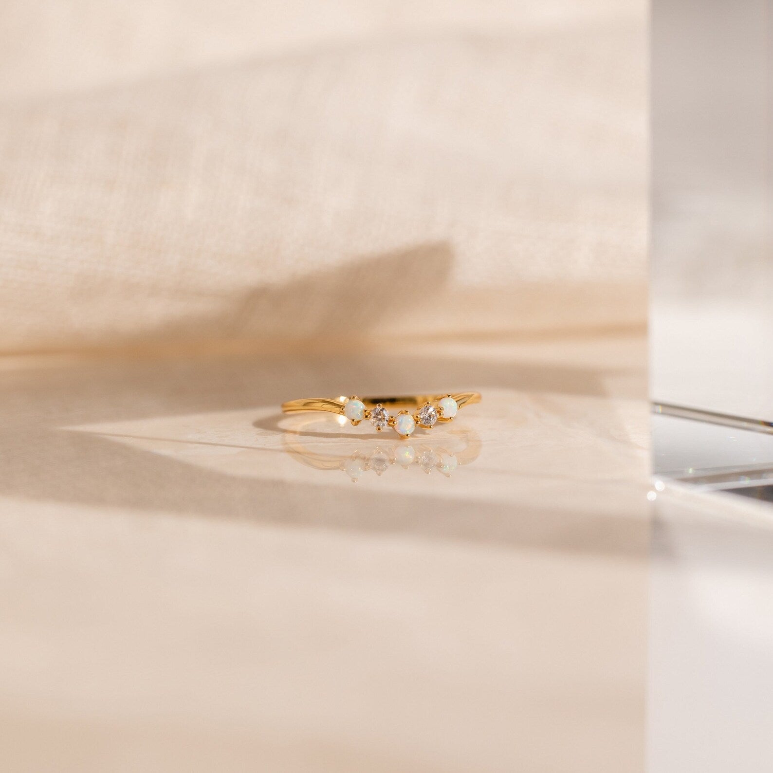 The Layla Opal Diamond Ring is a gold minimalist piece with delicate white gemstones, shown on a reflective surface against a soft beige background—ideal for a subtle boho chic ring statement.