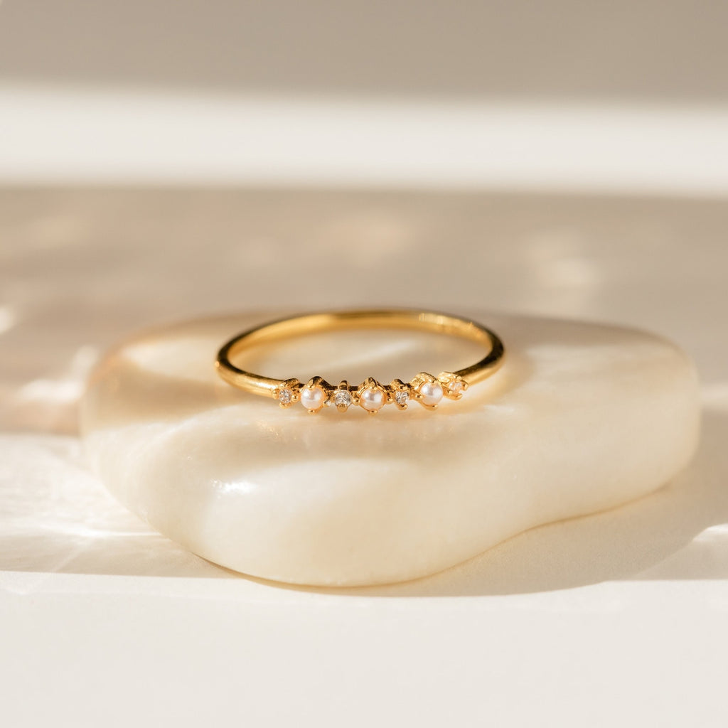 The Delicate Pearl Diamond Ring features petite pearls and diamonds set in gold, displayed on a cream stone—making it an ideal vintage engagement ring or a stylish stacking piece.