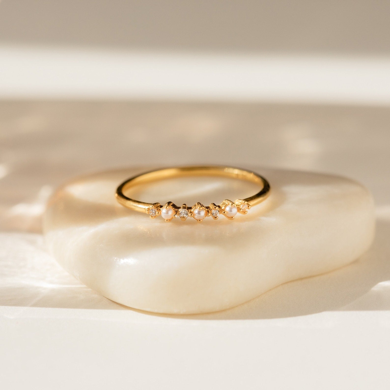 The Delicate Pearl Diamond Ring features petite pearls and diamonds set in gold, displayed on a cream stone—making it an ideal vintage engagement ring or a stylish stacking piece.