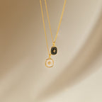 The Hermoine Pendant Necklace features two gold chains with square pendants—one black, one white—set against a neutral background, ideal for layering or pairing with your favorite Mother of Pearl piece.