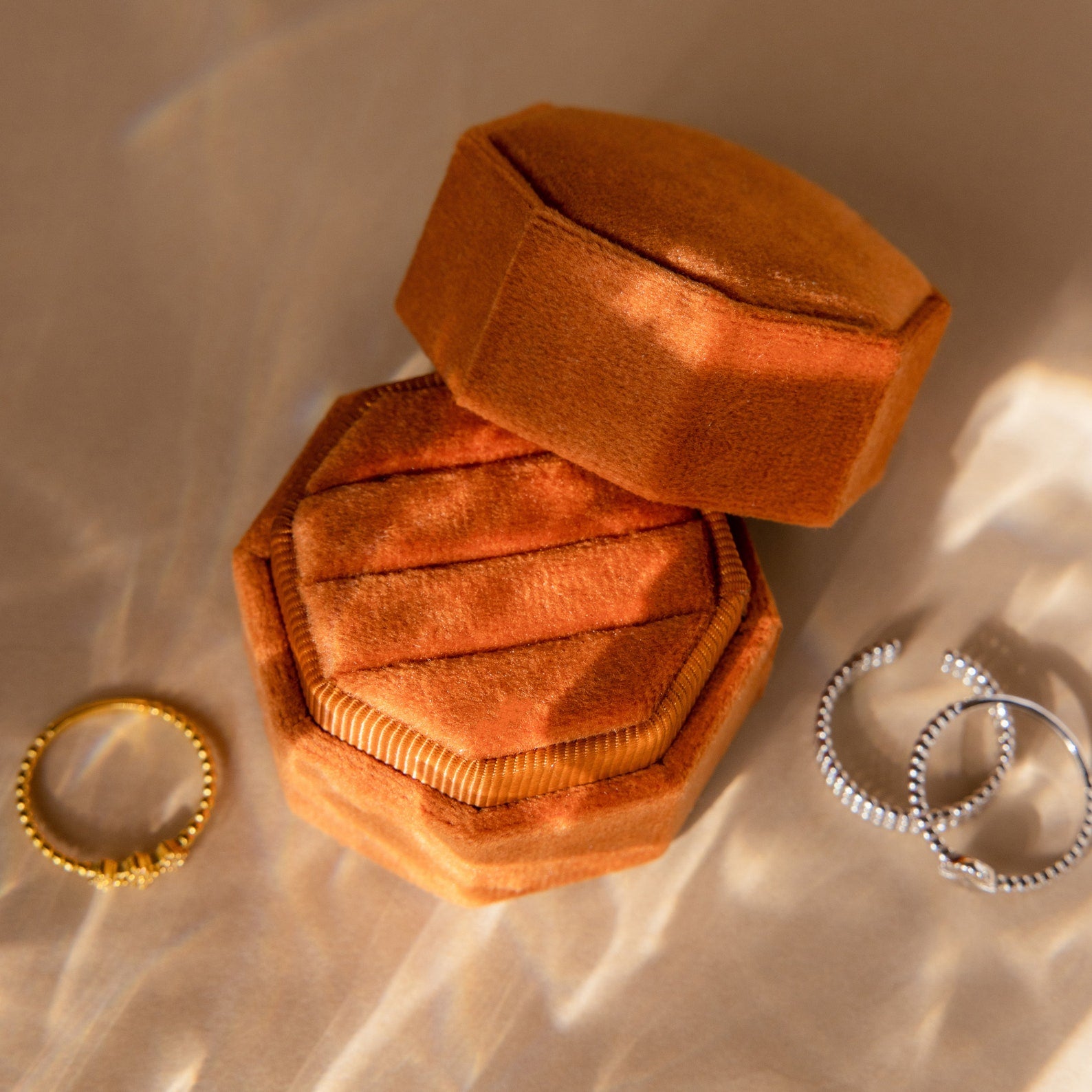 3 Slot Velvet Ring Box with lid off, surrounded by three rings on a beige surface—a chic organizer to stylishly display and protect your cherished jewelry pieces.