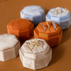 The Mystery Ring Box, available in tan, orange, and blue velvet, showcases gold and silver rings on a brown surface—each case adds elegance to your jewelry collection.