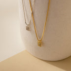 Two Mini Fingerprint Tag Necklaces, one silver and one gold, hang on a textured white ceramic vase—a meaningful personalized necklace and thoughtful Mother’s Day gift.