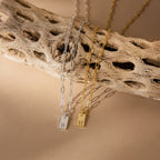 Two Mini Initial Paperclip Necklaces—one silver with an R and one gold with an H pendant—are displayed on a textured branch for a personalized touch.