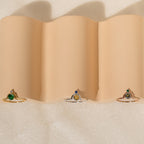 The Duo Vintage Birthstone Ring with colored center stones rests on wavy beige fabric—an elegant personalized mom ring, ideal for Mother’s Day or as a thoughtful gift for new moms.